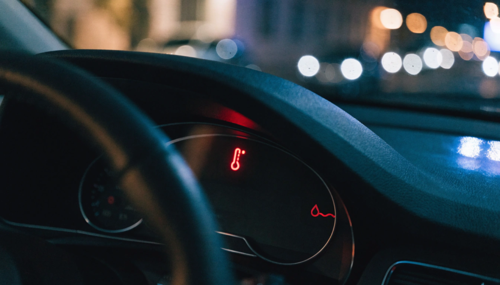 Close-up of an Audi dashboard displaying the red coolant temperature warning light at night.